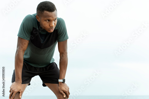 Multiracial jogger standing at the seashore while relaxing after hard training