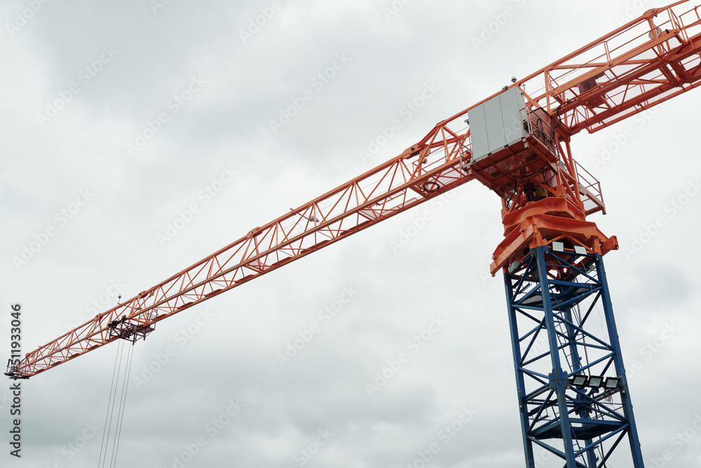 Part of huge high automatic tower crane with long red metallic jib used at construction site for building modern highrise condominium Part of huge high automatic tower crane with long red metallic jib used at construction site for building modern highrise condominium