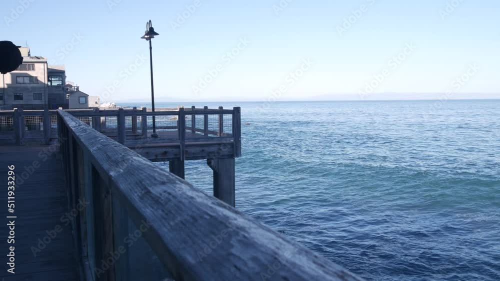 Waterfront wooden boardwalk in Monterey, California USA. Beachfront promenade on piles, pillars or pylons by ocean sea water and bay aquarium on Cannery Row street. Tourist vacations waterside resort. Waterfront wooden boardwalk in Monterey, California USA. Beachfront promenade on piles, pillars or pylons by ocean sea water and bay aquarium on Cannery Row street. Tourist vacations waterside resort.