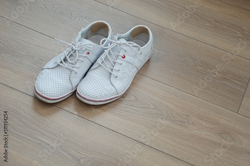 A pair of stylish sports shoes on a brown wooden floor. Inserts on the back of the shoe from calluses on the heels.