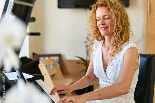 Woman in white dress sitting at the piano. Practice at home.