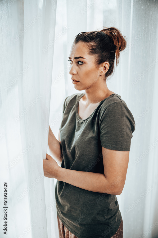 Woman Feeling Worried While Standing Near The Window At Home Woman Feeling Worried While Standing Near The Window At Home
