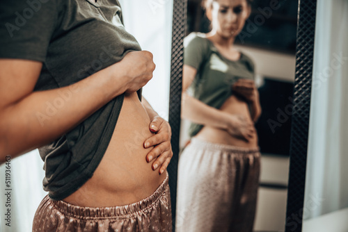 Woman Touching Her Belly While Standing Near Mirror photo