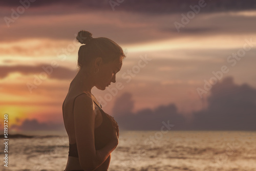 Young woman on sunset does yoga for healthy lifestyle on tropical sea or ocean beach outdoors