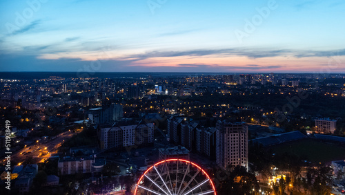Aerial view on vivid evening cityscape, city residential buildings development with Ferris wheel attraction in sunset. Kharkiv city center in sunset colors, Ukraine