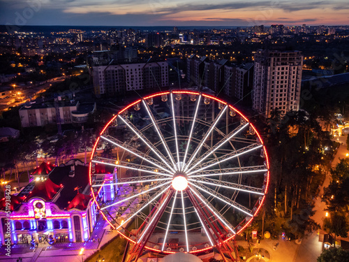 Aerial illuminated Ferris wheel close view. Kharkiv city center recreation area in evening lights. Amusement Gorky Central Park in sunset colors