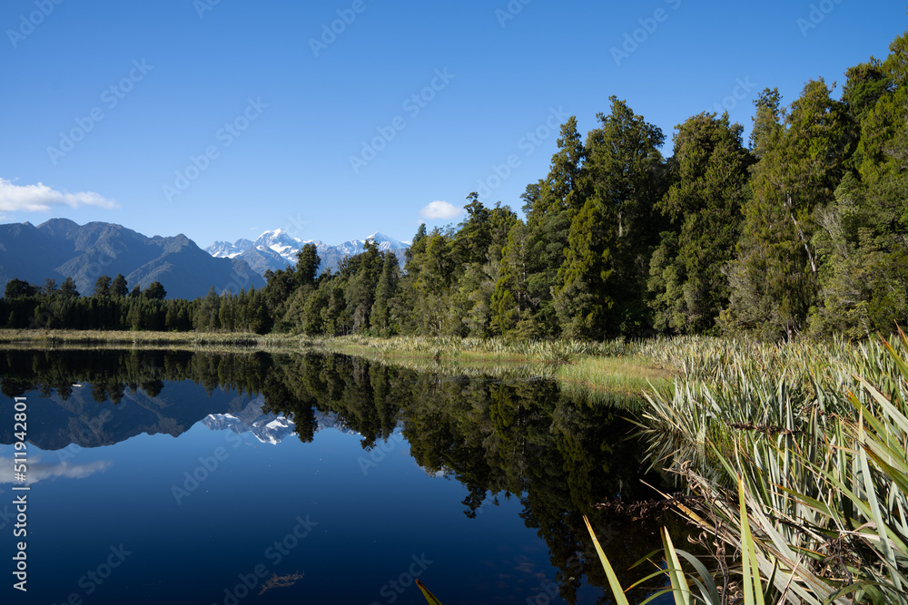 Leading line of forest edge of Lake matheson with Southern Alps and perfect reflection