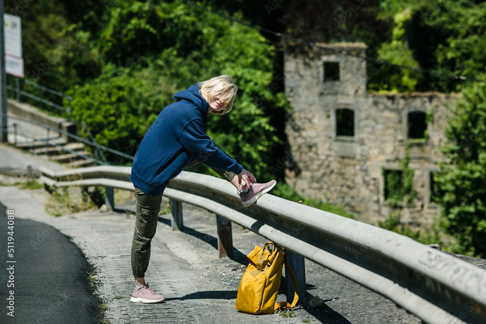 A female hiker with a yellow backpack is tying her shoelaces on the road. A female hiker with a yellow backpack is tying her shoelaces on the road.