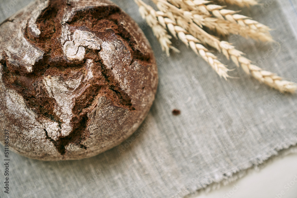 Top view of freshly baked rye bread on a yeast-free starter and on a mixture of whole grain, rye and wheat flour. It lies on a napkin, next to a dried flower with grains. Top view of freshly baked rye bread on a yeast-free starter and on a mixture of whole grain, rye and wheat flour. It lies on a napkin, next to a dried flower with grains.