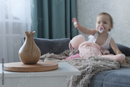 Aromatherapy concept. Little cheerful european girl with blond hair at home with a diffuser. Wooden Electric Ultrasonic Diffuser and Essential Oil Aroma Humidifier. Ultrasonic mini aroma diffuser for 