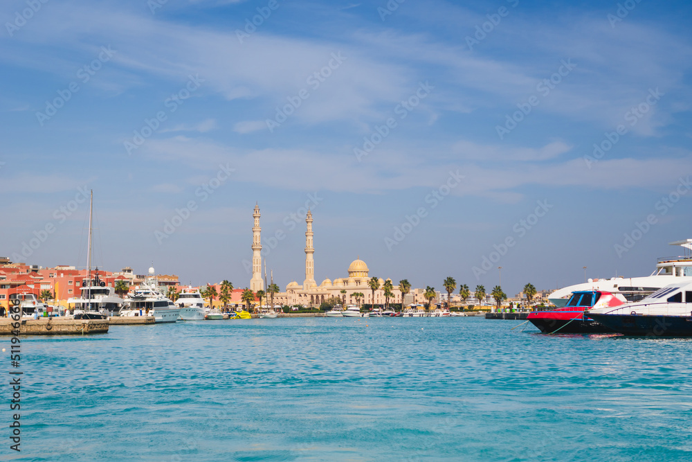Panoramic view from the sea in Hurghada to the minarets of the El Mina mosque and the city's embankment with moored yachts, shops, cafes and a pedestrian zone for walking