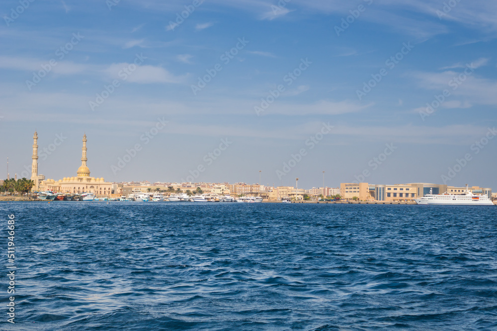 Panoramic view from the marina of Hurghada to the minarets of the El Mina mosque and the city's embankment with moored yachts, shops, cafes and a pedestrian zone for walking