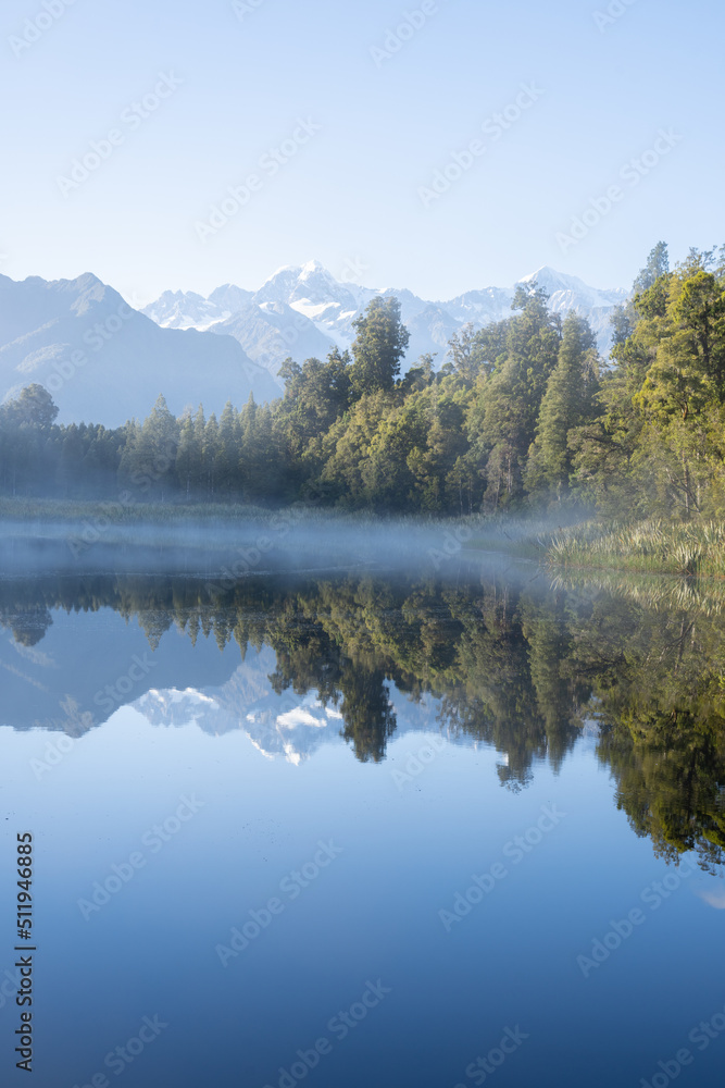 Perfect reflection in Lake Matheson surrounded by beautiful natural forest under blue sky