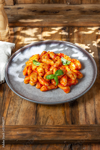 Close up of Italian potato Gnocchi with tomato sauce and fresh basil on gray plate on wooden background.