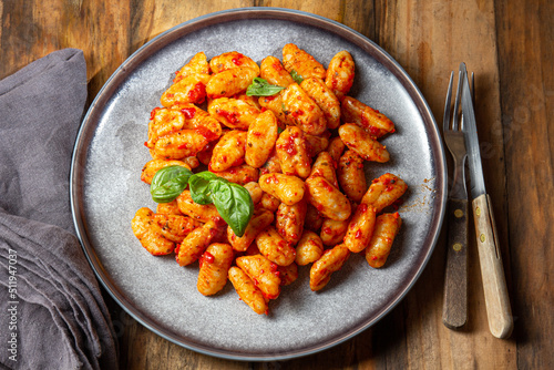 Traditional Italian potato Gnocchi with tomato sauce and fresh basil on blue plate on wooden background.