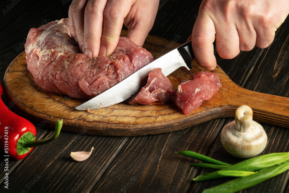 Chef hands cutting raw veal on a cutting board before cooking. Free space for advertising