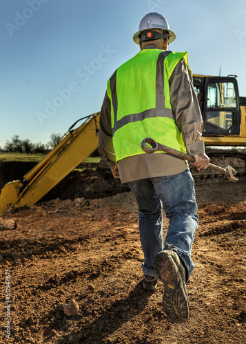 Heavy equipment mechanic operator working on an excavator with a large wrench. 