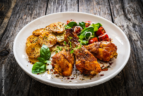 Barbecue chicken drumsticks with fried potato, lettuce and mini tomatoes on wooden table 