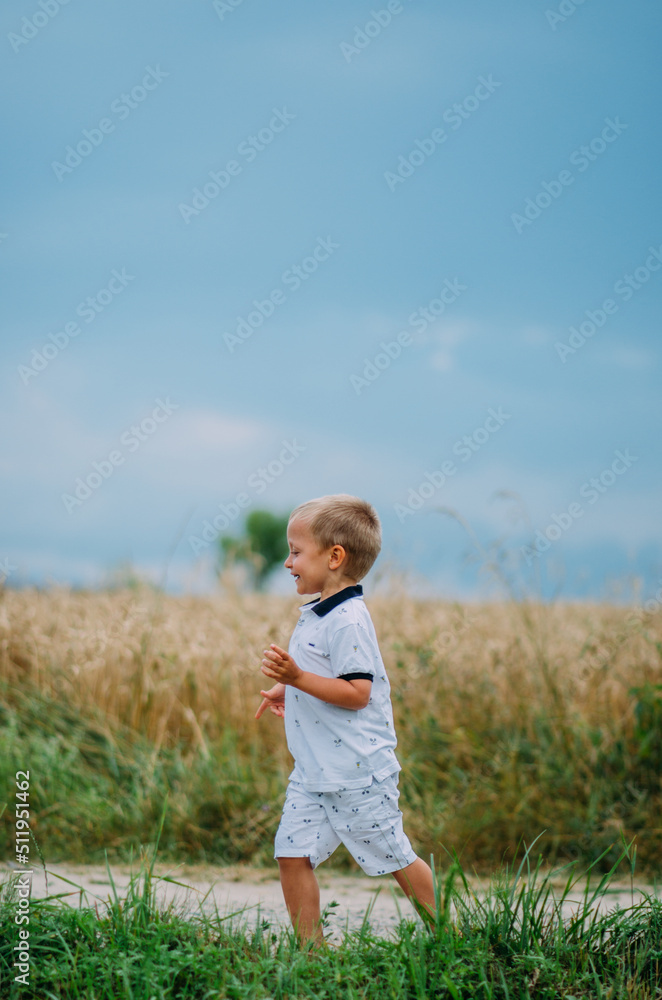 The boy runs against the background of a wheat field and blue sky. Ukrainian land. Child in nature. Relaxation. The boy runs against the background of a wheat field and blue sky. Ukrainian land. Child in nature. Relaxation.
