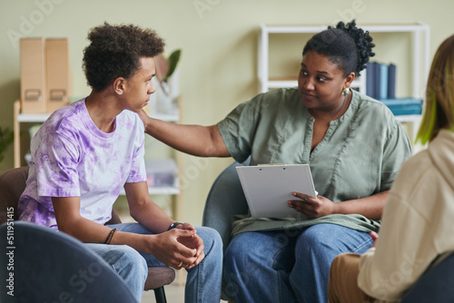 African young psychologist talking to teenage boy during therapy session at clas Fototapeta