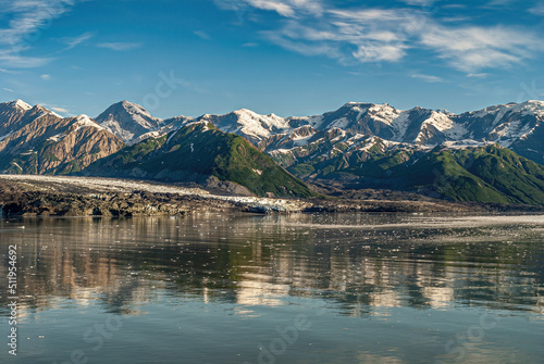 Disenchantment Bay, Alaska, USA - July 21, 2011: Not that much ice at Turner Glacier landing under blue cloudscape. Snow topped mountain range on horizon and mirrored in ocean water.