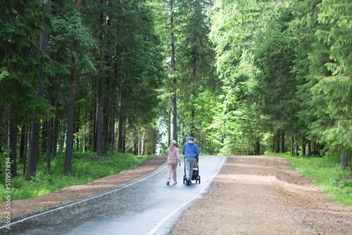 A family, a man and a woman with a child in a baby carriage walk in the park in summer.