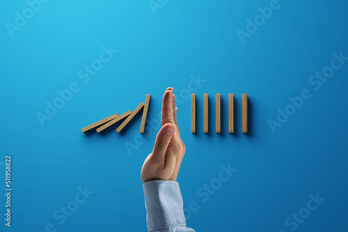 A hand stops the tipping over of wooden dominoes. Concept of containment of problems.
