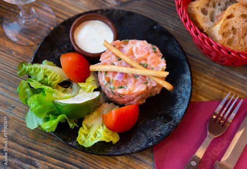 National French appetizer salmon tartare with onion cream, served with sauce, fresh tomato, lime and lettuce leaves photo