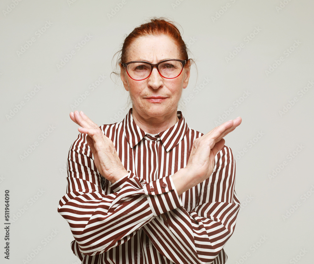 Elderly woman wearing striped shirt and eyeglasses rejection expression crossing arms doing negative sig Elderly woman wearing striped shirt and eyeglasses rejection expression crossing arms doing negative sig