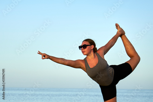 Young healthy woman practicing and workout yoga on the beach at sunset, benefits of natural environments for physical activity.