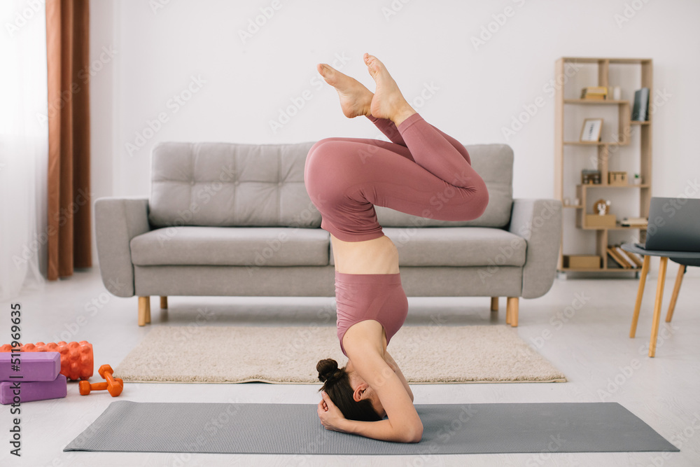 Attractive young woman stands on her head and upside down and doing fitness exercises at home. Attractive young woman stands on her head and upside down and doing fitness exercises at home.