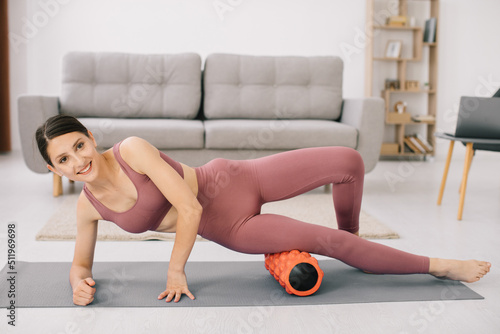 Attractive young sports woman doing exercises on the abdomen with a roller at home.