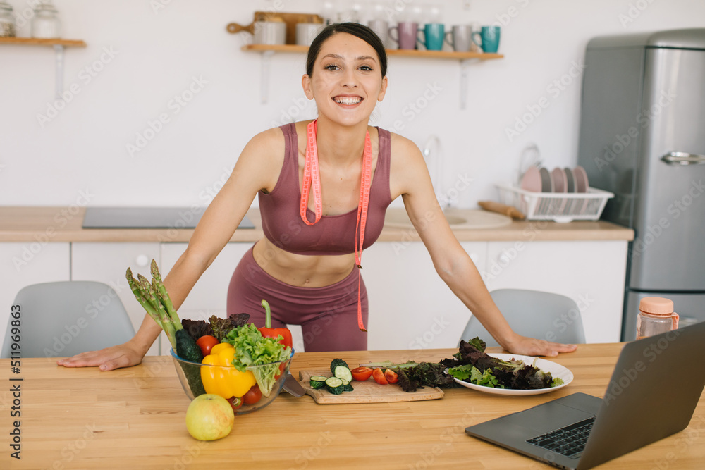 Portrait of sporty woman blogger leading video conference on healthy eating on laptop in kitchen Portrait of sporty woman blogger leading video conference on healthy eating on laptop in kitchen
