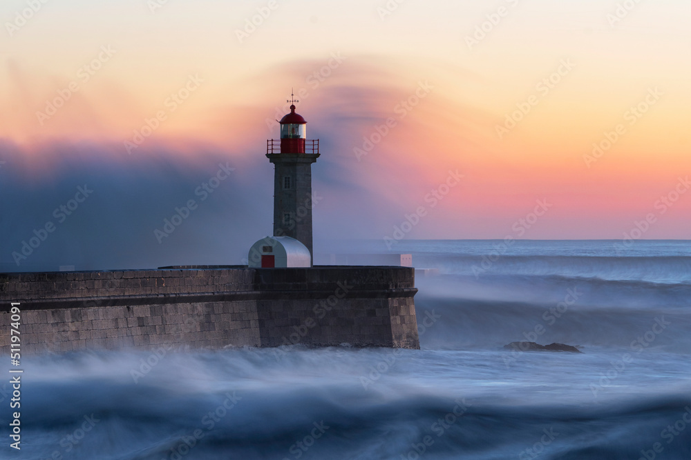 Long exposure of lighhouse being hit by a wave at sunset