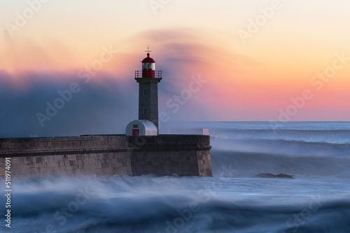 Long exposure of lighhouse being hit by a wave at sunset photo
