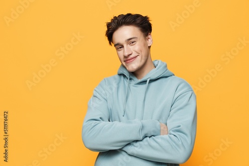 a close horizontal photo of a handsome young man standing on an orange background in a light blue hoodie with his arms crossed over his chest © Tatiana