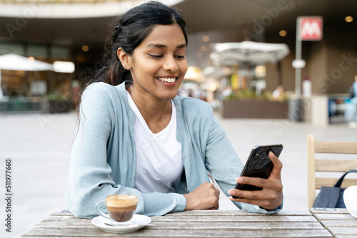 Smiling Indian woman holding cell phone communication online, reading text message sitting in cafe. Asian female using mobile app shopping online. Modern technology,
E-commerce 