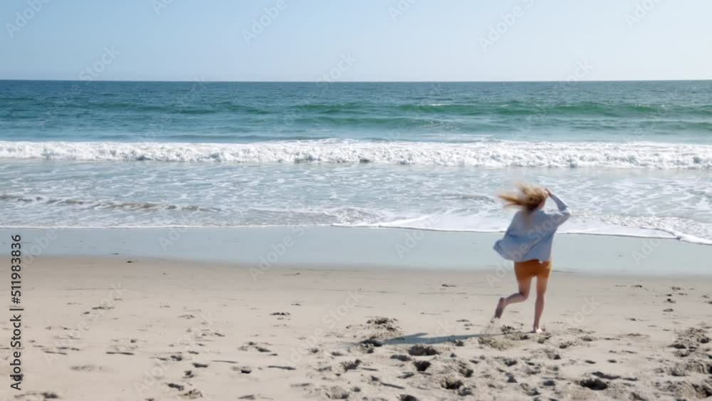 Cheerful and happy woman running towards the sea. Astonishing natural landscape with sandy beach and endless ocean with foamy waves as seen from the shore. High quality 4k footage Cheerful and happy woman running towards the sea. Astonishing natural landscape with sandy beach and endless ocean with foamy waves as seen from the shore. High quality 4k footage