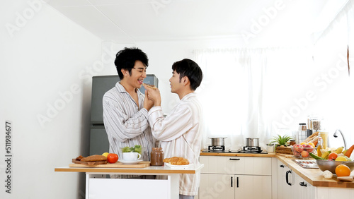 Happy gay couple enjoy breakfast in kitchen drinking coffee. Two best friends LGBTQ relation partner home cooking. Happiness romance homosexual marriage lifestyle. Two men together love friendship.