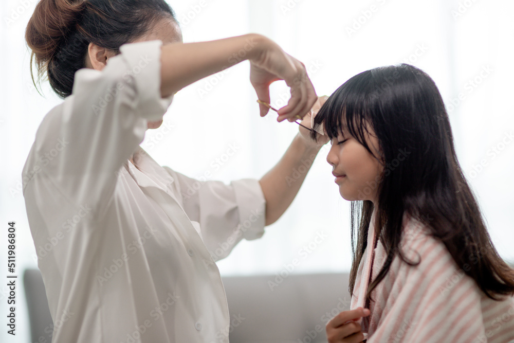Asian Mother cutting hair to her daughter in living room at home while stay at home safe from Covid-19 Coronavirus during lockdown. Self-quarantine and social distancing concept. Asian Mother cutting hair to her daughter in living room at home while stay at home safe from Covid-19 Coronavirus during lockdown. Self-quarantine and social distancing concept.