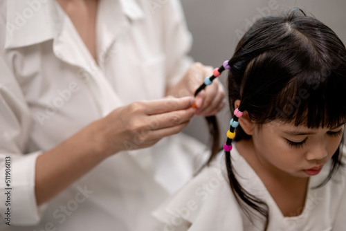 Young Asian mother tying daughter's hair