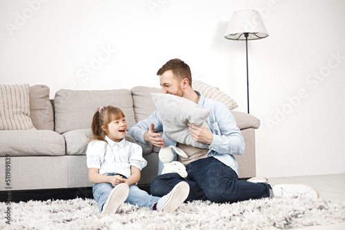 Girl with Down syndrome and her father sitting on a floor and talkiing together