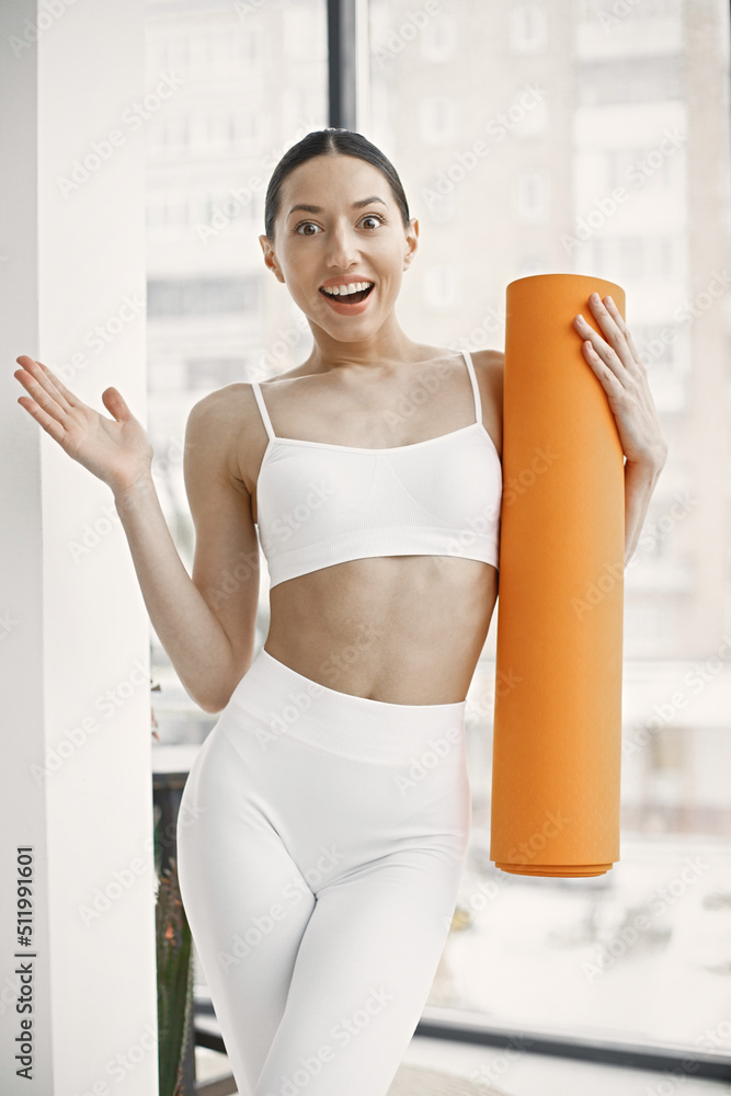 Young fitness woman ready for workout holding orange yoga mat