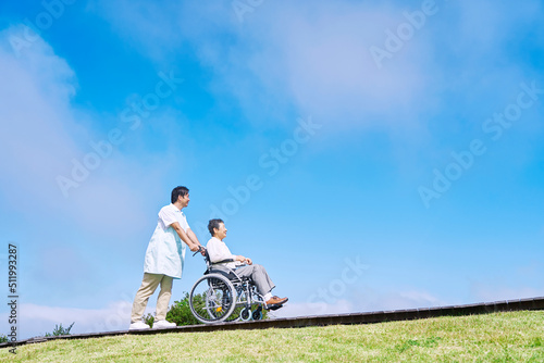 看護師と屋外を車椅子に乗って散歩する高齢者女性