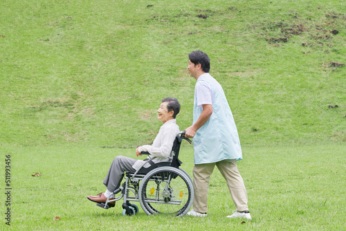 看護師と屋外を車椅子に乗って散歩する高齢者女性