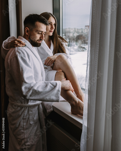 Couple wearing bathrobes in hotel standing near window