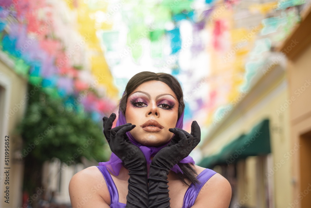 Drag Queen street portrait with multicolor background. Young man dressed as a woman looking at the camera.