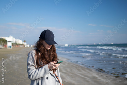 Woman in a black cap is using smartphone near the sea © Yurii Kushniruk