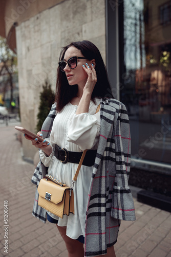 Pretty stylish brunette female calling on cellphone at street in town. Business lady.