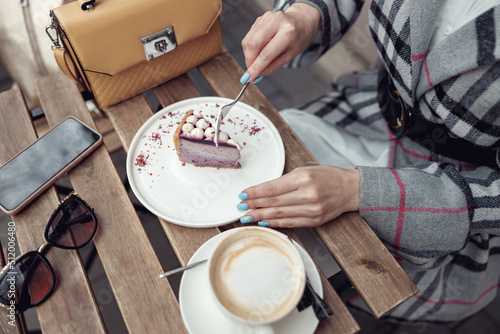 Top view on female with blue manicure eating cheesecake with cappuccino at table outside.  photo